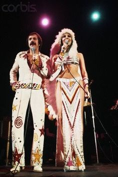 two people standing on stage with microphones in their hands and one person wearing costume