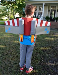 a young boy wearing an airplane costume standing in front of a house with his back to the camera