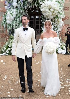 a bride and groom holding hands in front of an archway decorated with white flowers at their wedding