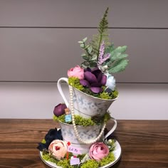 three tiered teacups with flowers and moss on the top, one is filled with beads