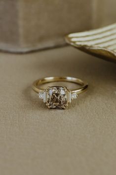 a gold ring with a brown and white diamond in it sitting on a beige surface