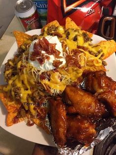 a white plate topped with chicken wings and nachos covered in cheese next to chips