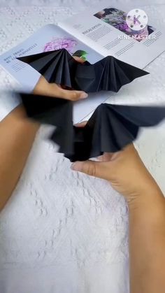 two hands holding folded black paper in front of an open book on a white surface