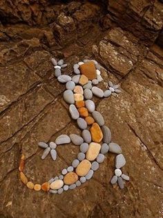 a lizard made out of rocks sitting on top of a rock covered ground next to a tree