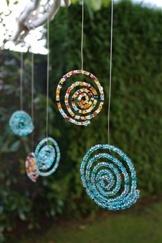 some colorful beads hanging from a tree in front of a fence and bushes with green grass