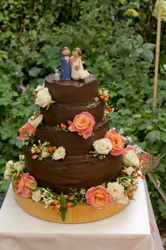 a three tiered chocolate wedding cake with flowers on the side and a bride and groom figurine on top