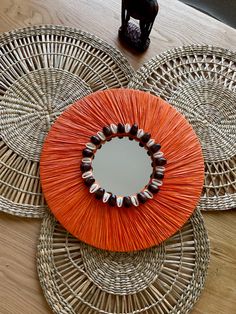 an orange circular mirror sitting on top of a wooden table next to a black vase