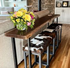 a wooden table topped with a vase filled with flowers next to two stools covered in cowhide