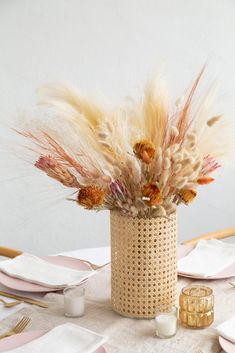 an arrangement of dried flowers in a vase on a table with place settings and napkins