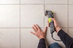 a person using a power tool on a tile floor in front of a white tiled wall