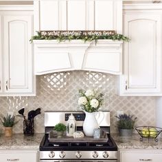 a kitchen with white cabinets and an oven in the center is decorated with greenery