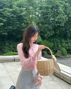 a woman holding a wicker basket in front of her face while standing on a stone walkway