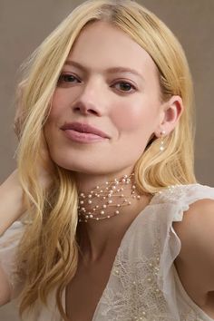 a woman with blonde hair wearing a white dress and pearls on her neck is posing for the camera