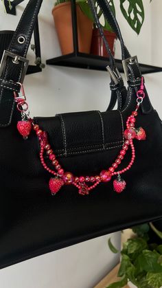 a black purse with pink beads and heart charms on the handle, hanging from a hook