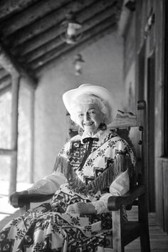 an old woman sitting in a rocking chair with a hat on her head and looking at the camera