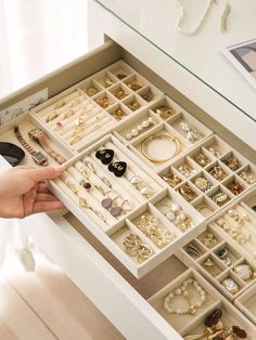 a drawer with many different types of jewelry in it and someone's hand reaching for them