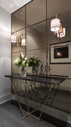 a glass table with vases and flowers on it in front of a mirror wall