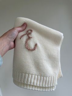 a hand holding a white knitted sweater with the letter c on it's side