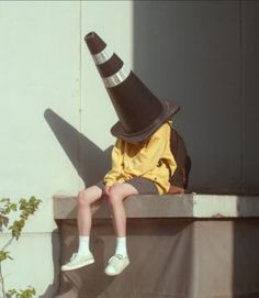 a young boy wearing a black and white hat sitting on top of a cement wall