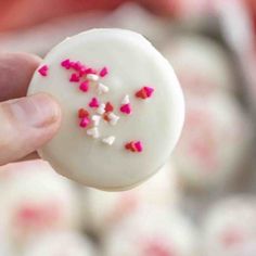 a hand holding a white frosted donut with pink and red sprinkles