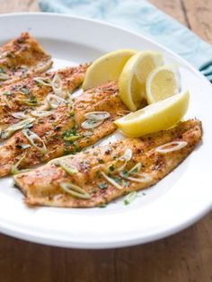 a white plate topped with fish next to lemon wedges and parmesan cheese