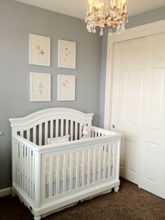 a baby's room with a white crib, chandelier and pictures on the wall