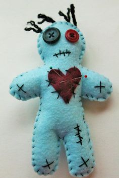 a blue teddy bear with a red heart on it's chest and two black pins in its mouth