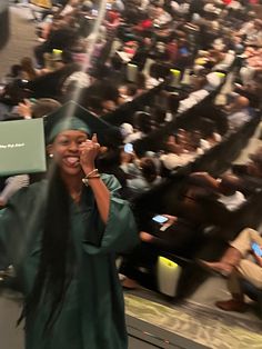 a woman in a graduation cap and gown holding up a laptop computer while standing in front of an auditorium full of people