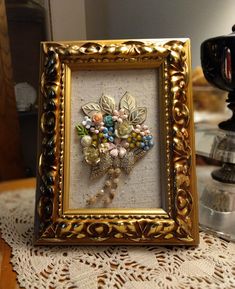 a gold frame with some beads in it on a lace doily next to a coffee pot