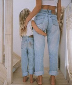 two women standing next to each other in jeans