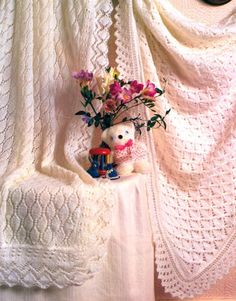 there is a white crocheted blanket with flowers in it and a teddy bear