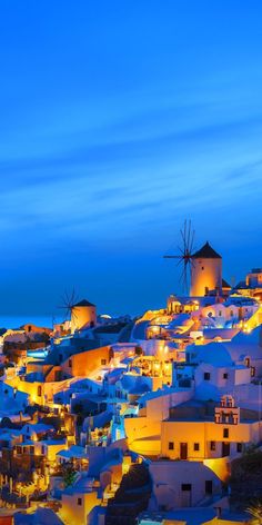 the city is lit up at night with bright lights on buildings and windmills in the background