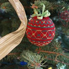 a red ornament hanging from the top of a christmas tree with green ribbon