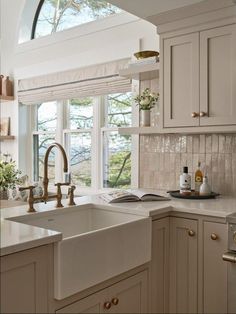 a kitchen with white cabinets and an arched window above the sink is filled with greenery