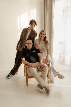 three people sitting on a chair in front of a window