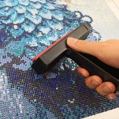 a hand holding a black and red object on top of a blue rug with flowers