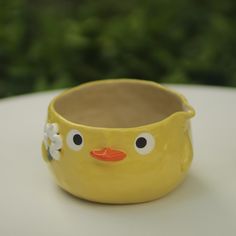 a yellow cup with a face painted on the side and flowers in its mouth, sitting on a white table