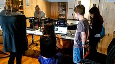 three people are standing in front of a computer screen while others look at the monitor