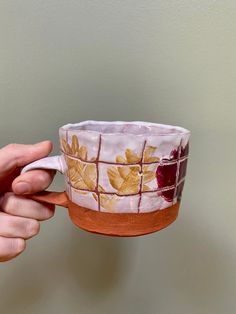 a hand holding a coffee cup that is decorated with leaves and red paint on it