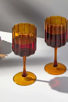 two wine glasses sitting on top of a white table next to each other with red and yellow liquids in them