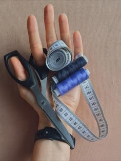 a hand holding scissors, measuring tape and thread