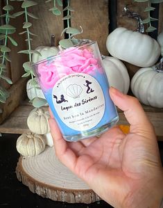 a hand holding a jar filled with pink and white marshmallows on top of a table