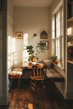 the sun shines through two windows onto a dining room table and bench with plants on it