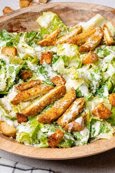 a wooden bowl filled with salad covered in cheese and bread croutons on top of a checkered table cloth