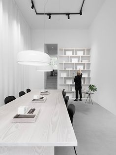 a long table with black chairs in front of a white book shelf and light fixture