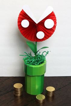 a red and white paper flower sitting on top of a green box next to coins