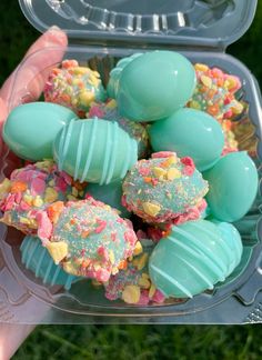 a person holding up a plastic container filled with colorful desserts on top of green grass