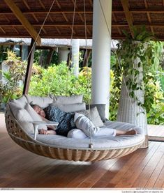 a woman laying on a hanging chair in the middle of a wooden floored porch