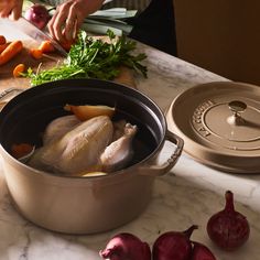 a person cutting up vegetables in a pot on a counter top with a turkey and carrots