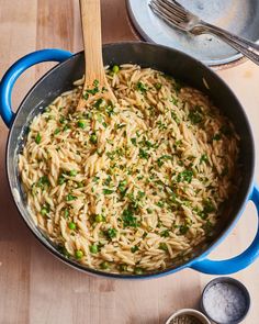 a blue pot filled with pasta and parsley on top of a wooden table next to measuring spoons